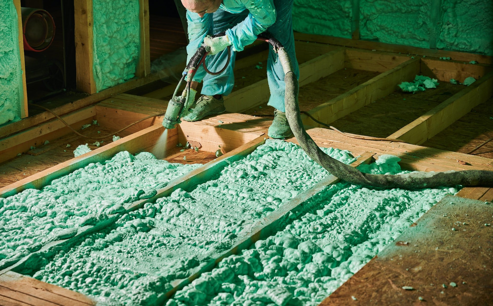 Worker spraying polyurethane foam for insulating wooden frame house.